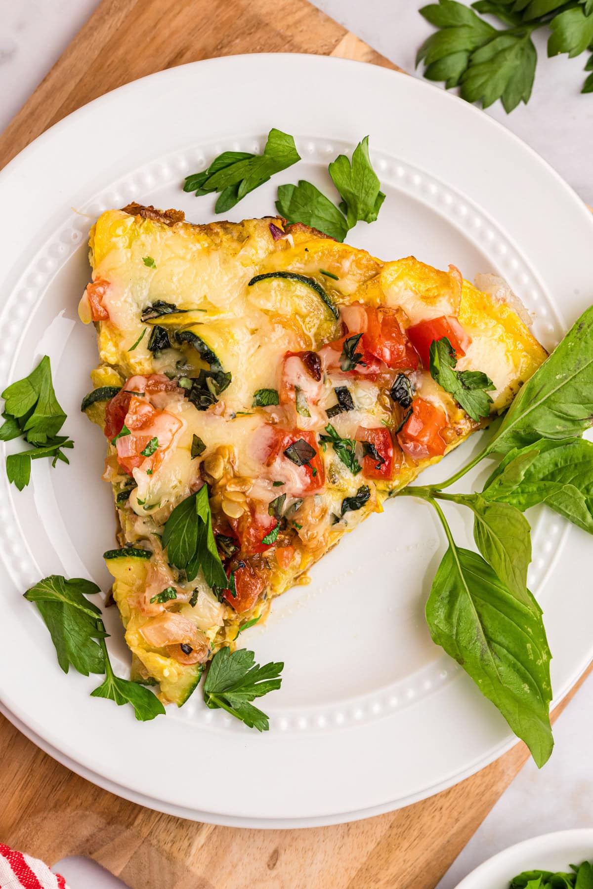 squash and tomato oven frittata slice on plate with basil leaves