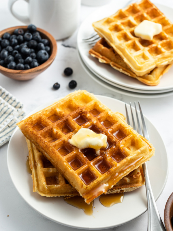 waffles stacked on plate with butter and syrup