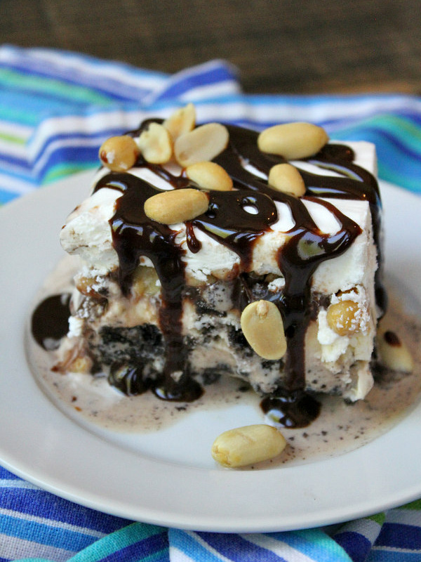 one slice of buster bars on a white plate and topped with fudge and peanuts. displayed on a blue/teal/white striped napkin