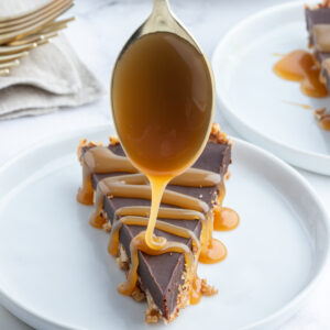 spooning caramel sauce on top of slice of chocolate pecan tart on plate