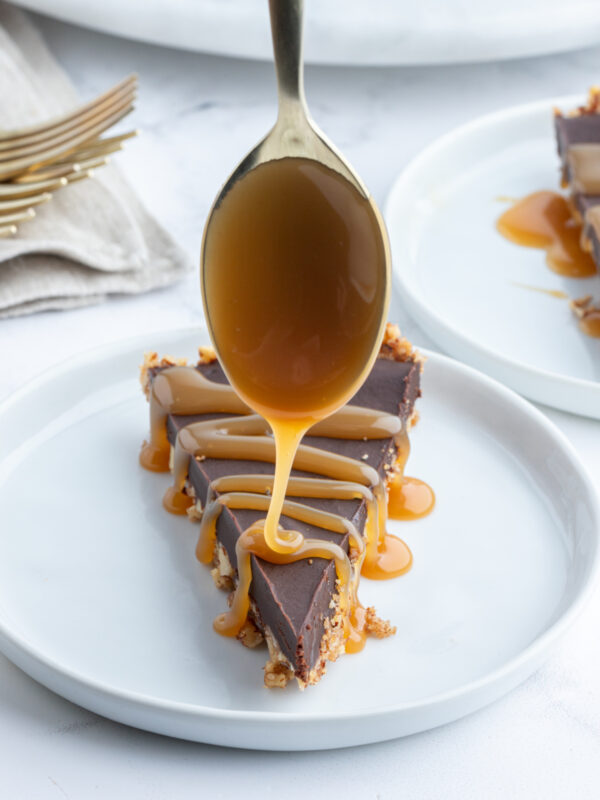 spooning caramel sauce on top of slice of chocolate pecan tart on plate