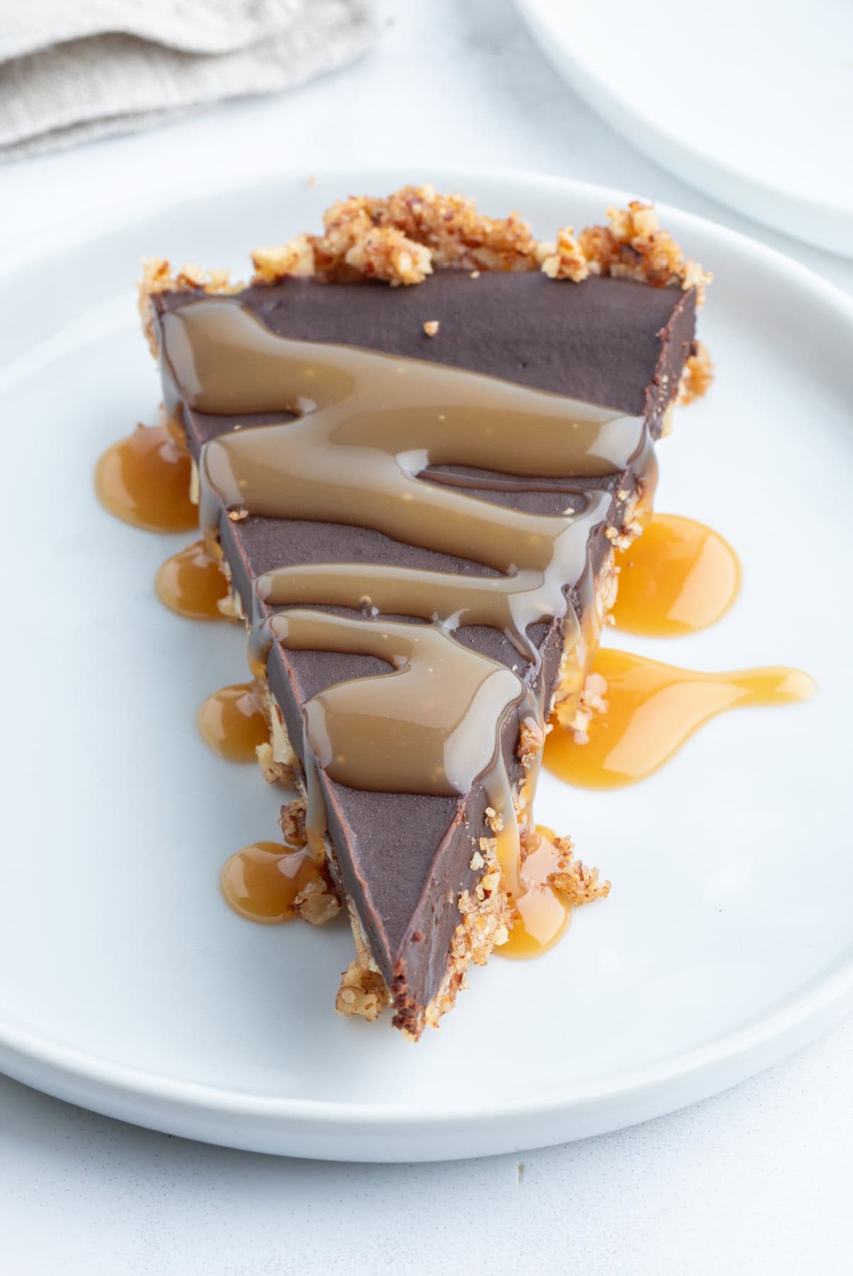 slice of chocolate pecan tart on plate topped with caramel sauce