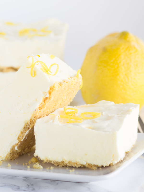 frozen lemon cheesecake squares displayed on white plate with a lemon