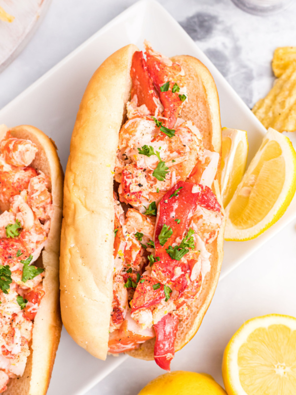 two lobster rolls on plate with lemon wedges