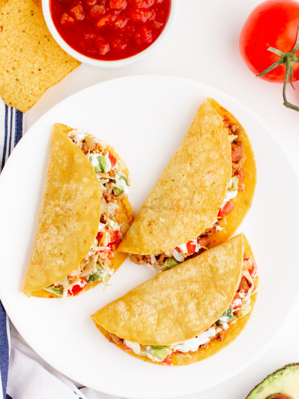 three tacos on a white plate with side of salsa