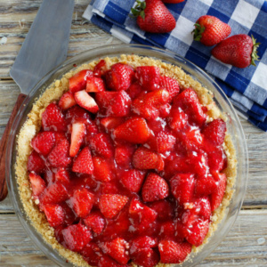 overhead shot of strawberry pie with blue/white checked napkin and fresh strawberries in background