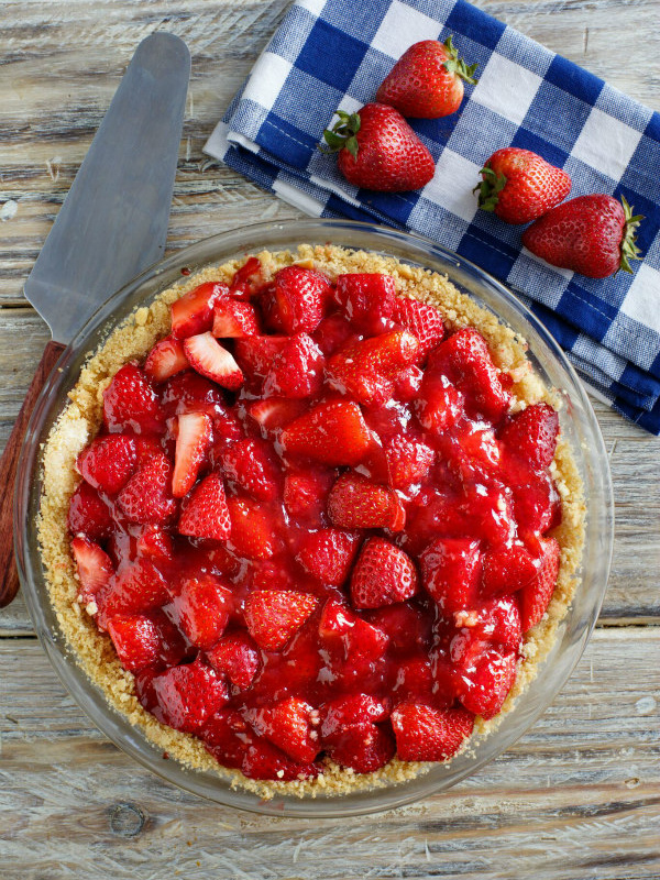 overhead shot of strawberry pie with blue/white checked napkin and fresh strawberries in background