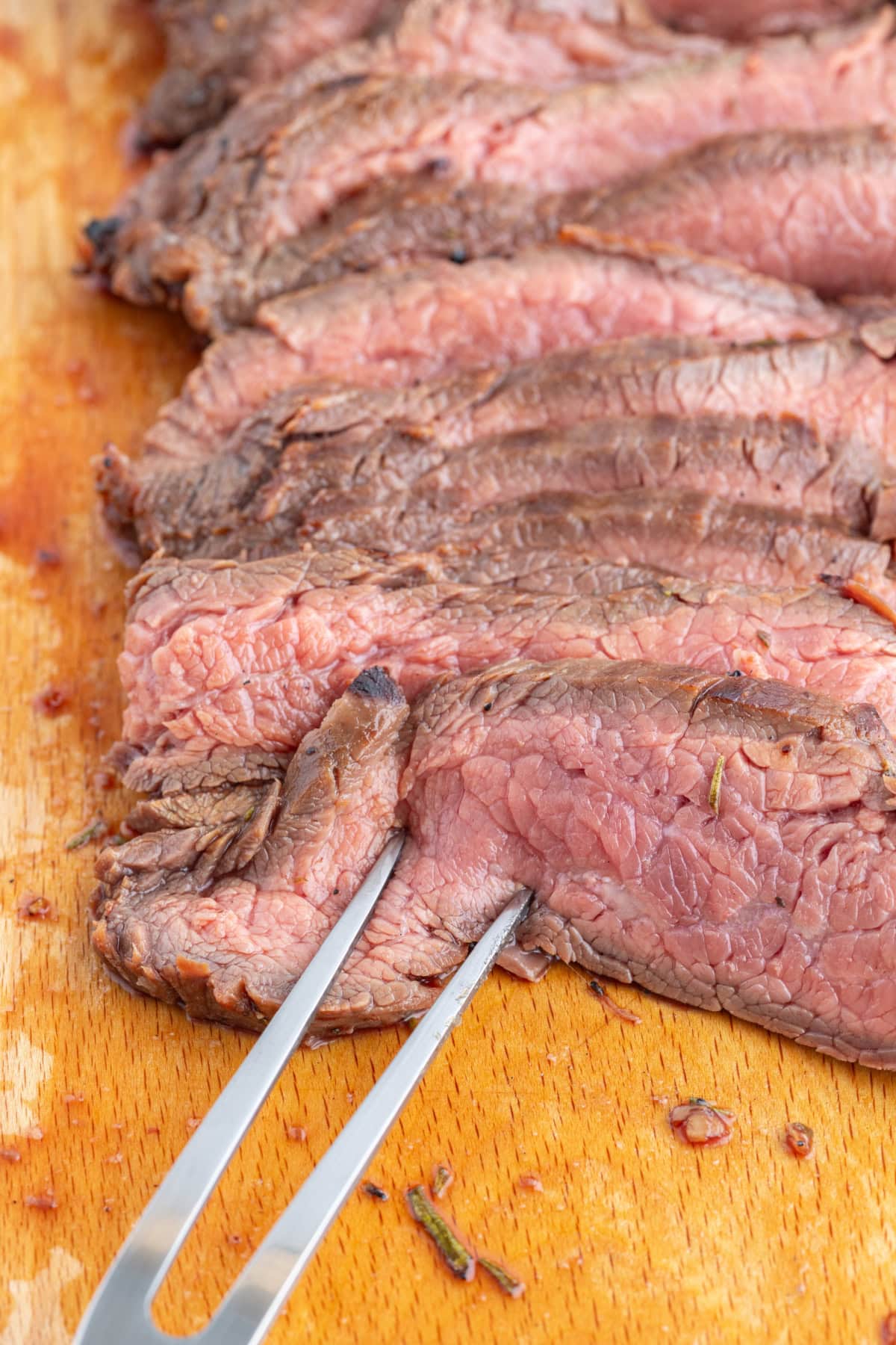 fork piercing slices of grilled flank steak on a board
