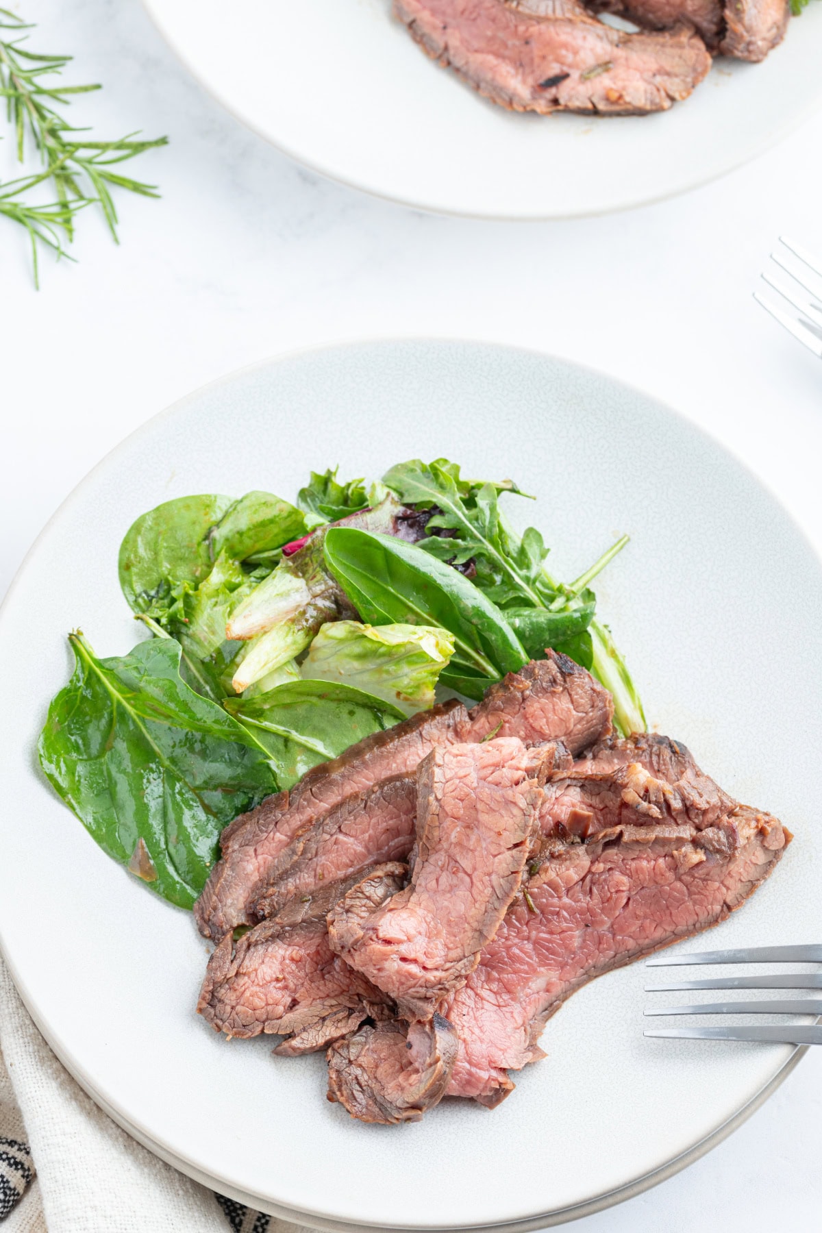 slices of grilled flank steak with rosemary marinade on plate with salad