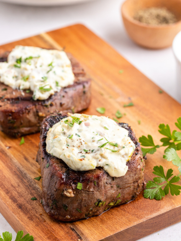 two steaks on a cutting board topped with blue cheese sauce