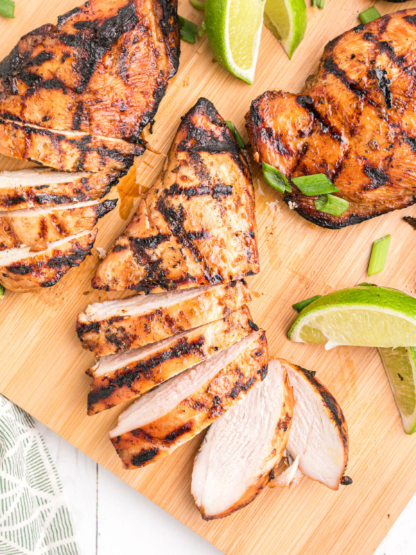 hoisin and lime marinated grilled chicken breasts on a board with lime wedges