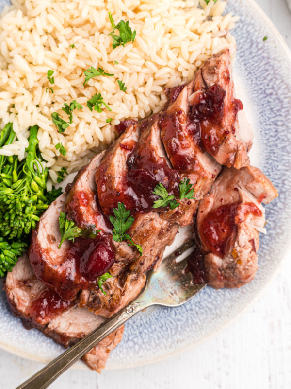 serving of orange cranberry glazed pork tenderloin on a plate with rice and broccoli