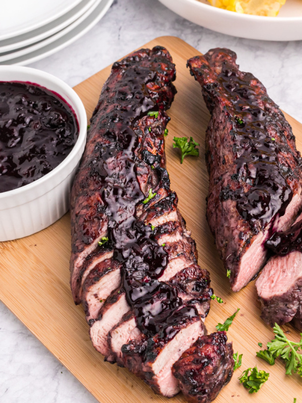 grilled pork tenderloin on a board topped with blueberry BBQ Sauce