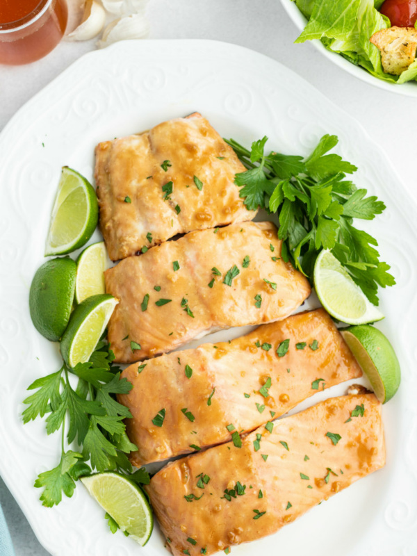 barbecued salmon cut into fillets and displayed on a white plate with parsley and lime wedges