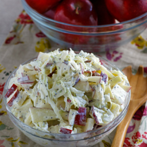 apple cole slaw in a bowl and apples in another bowl. wooden spoon on the side. set on a floral napkin