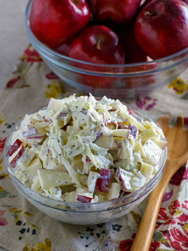 apple cole slaw in a bowl and apples in another bowl. wooden spoon on the side. set on a floral napkin