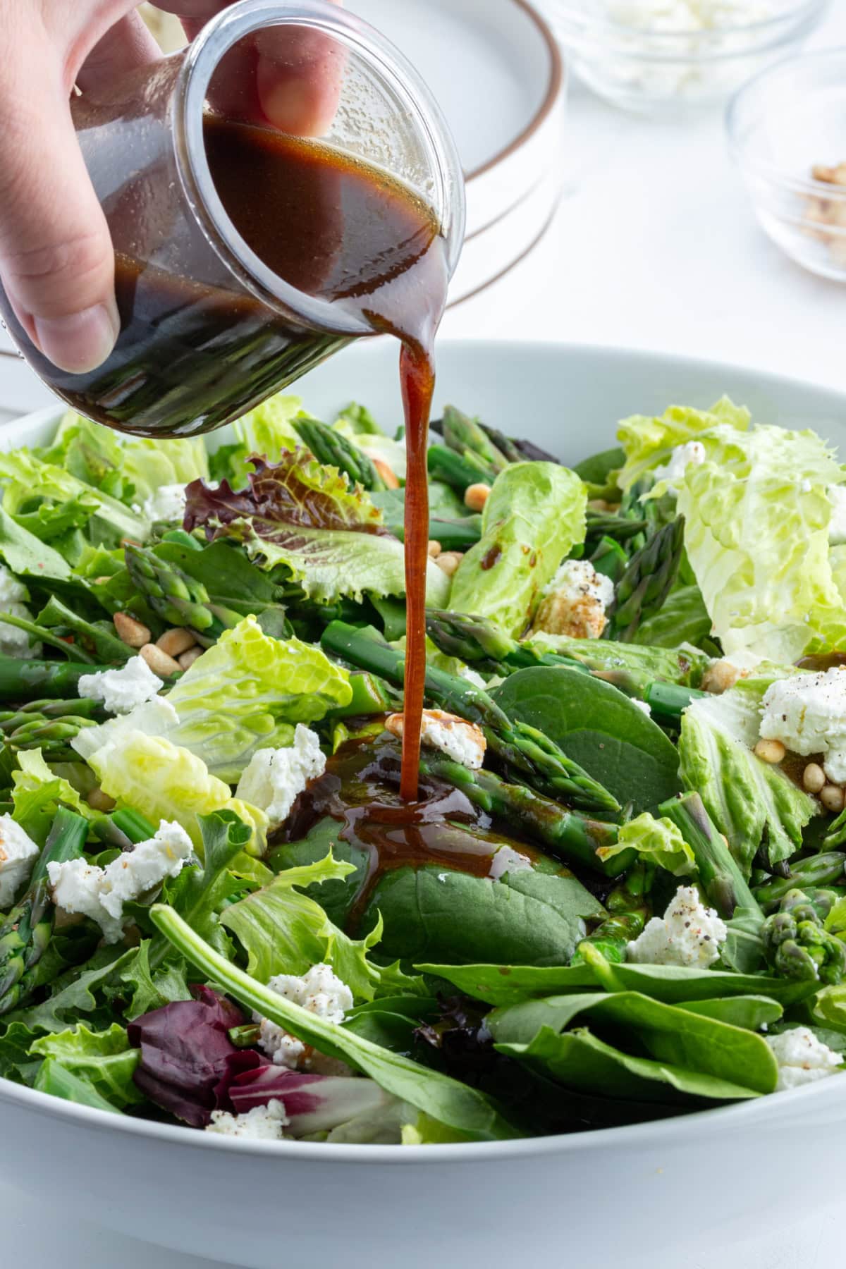 pouring dressing onto asparagus and goat cheese salad