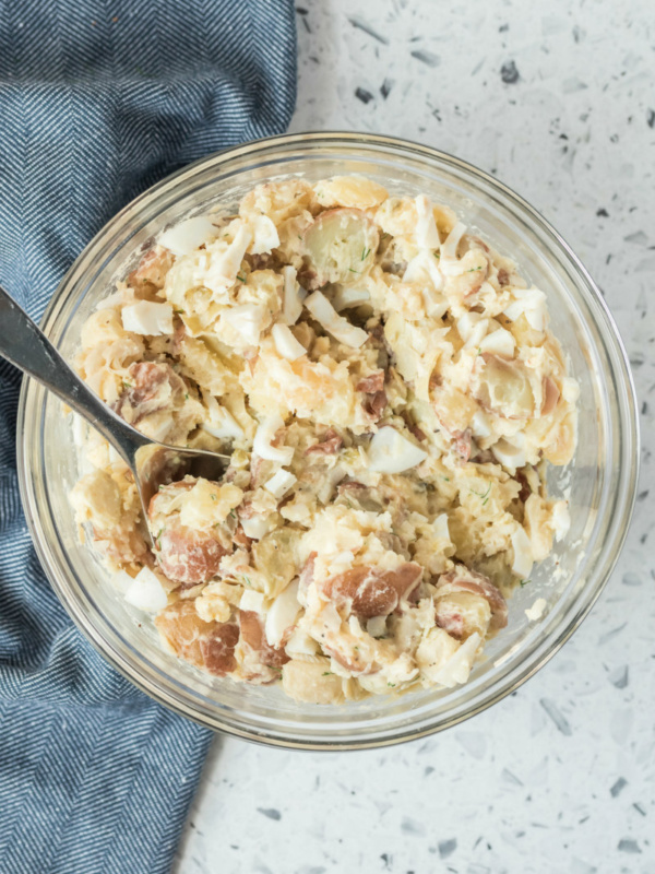 overhead shot of potato salad in a glass bowl with a serving spoon, set on a blue napkin