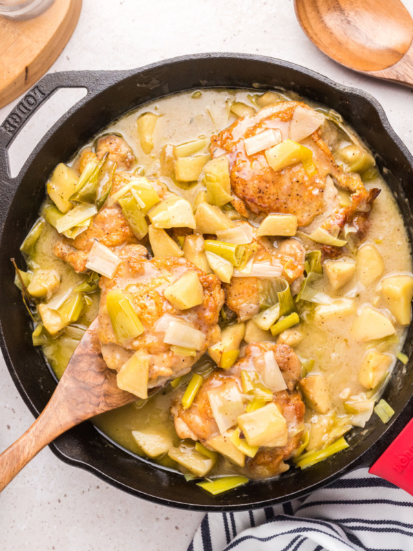 spooning chicken out of chicken, leek and apple stew in skillet