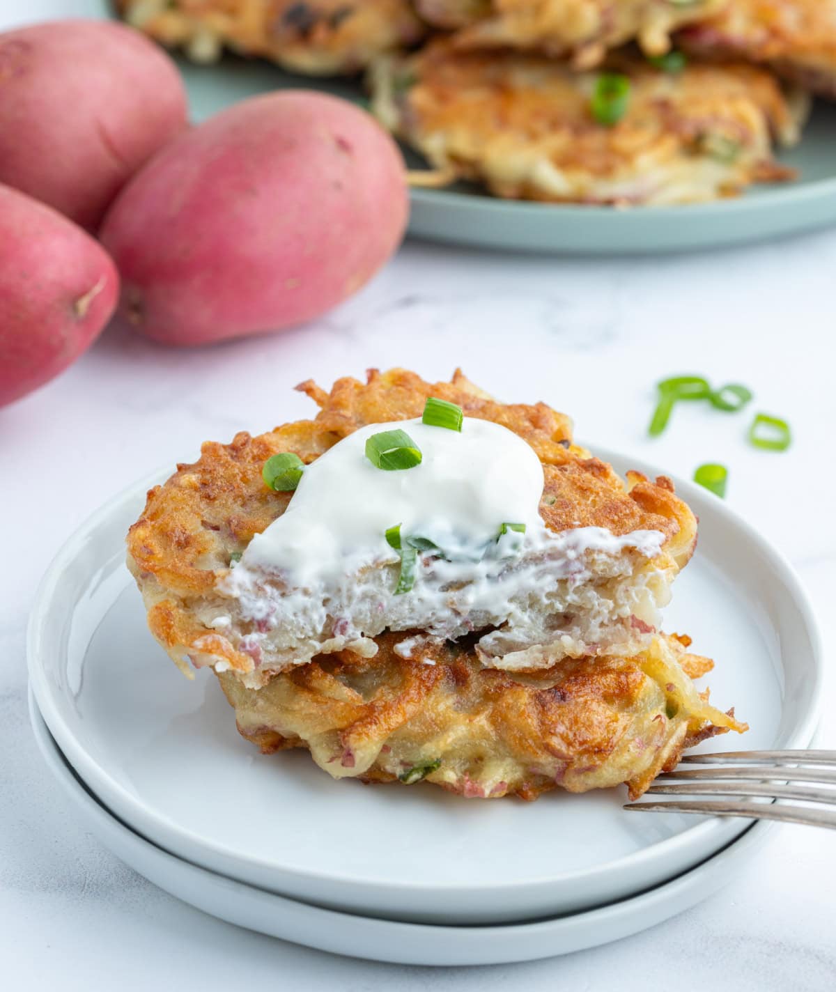 crispy potato pancakes stacked on plate and topped with sour cream and cut in half