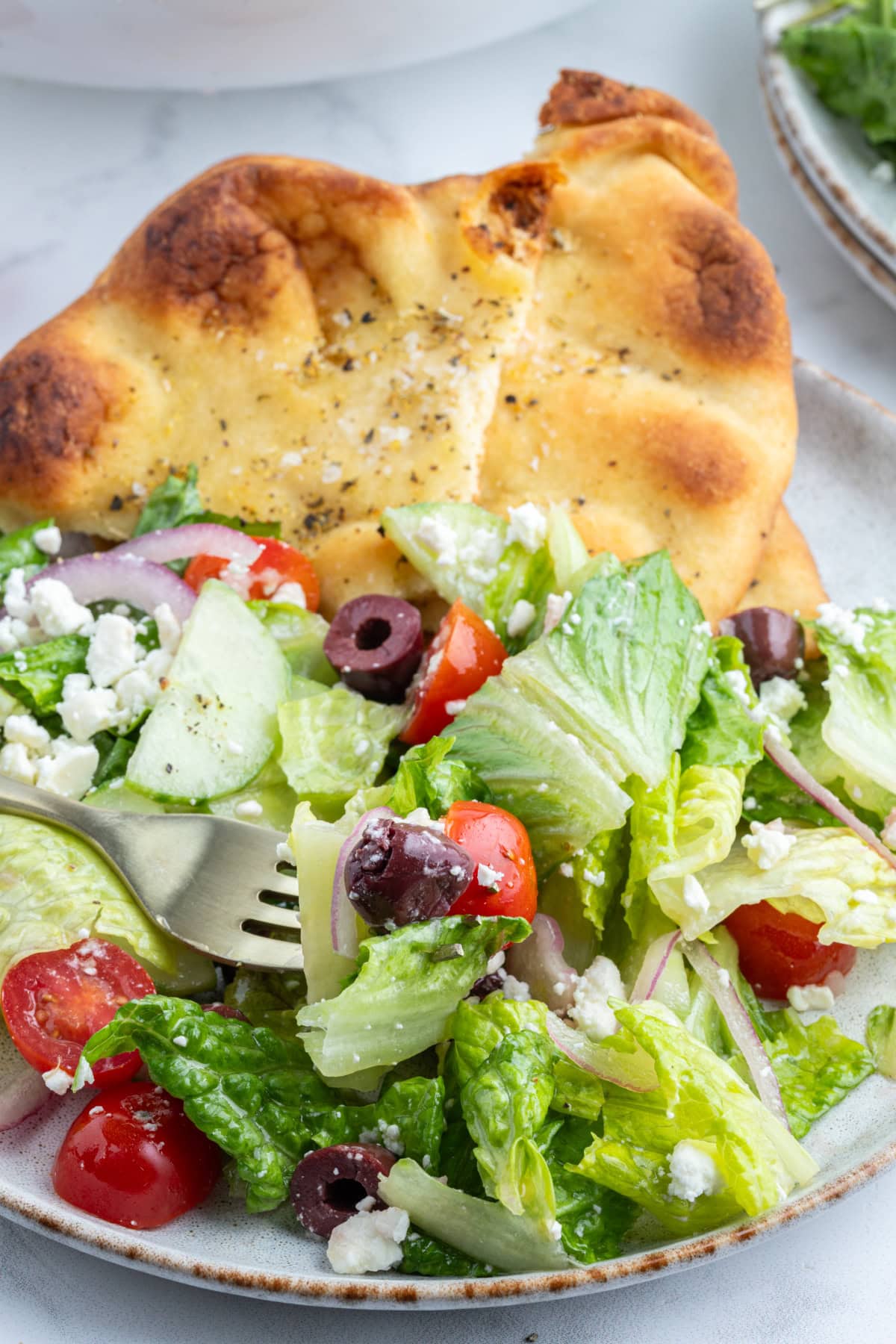 fork in a bowl of greek salad with seasoned flatbread