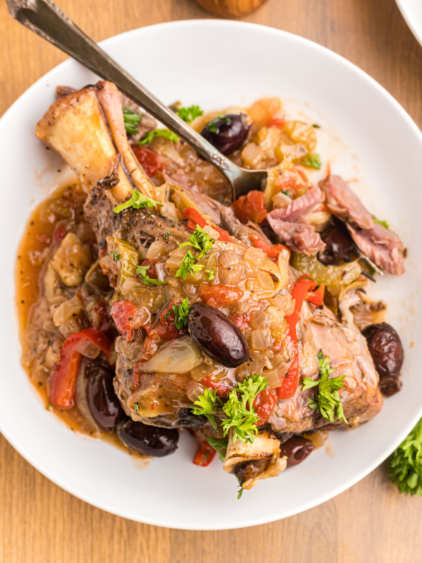 lamb shank on a plate topped with artichokes and olives