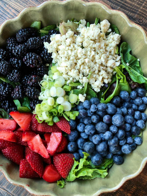 overhead shot of ingredients for triple berry salad set in a green bowl on a wooden surface