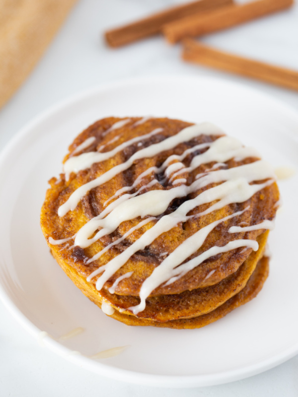 pumpkin cinnamon roll pancakes on plate with cream cheese glaze on top