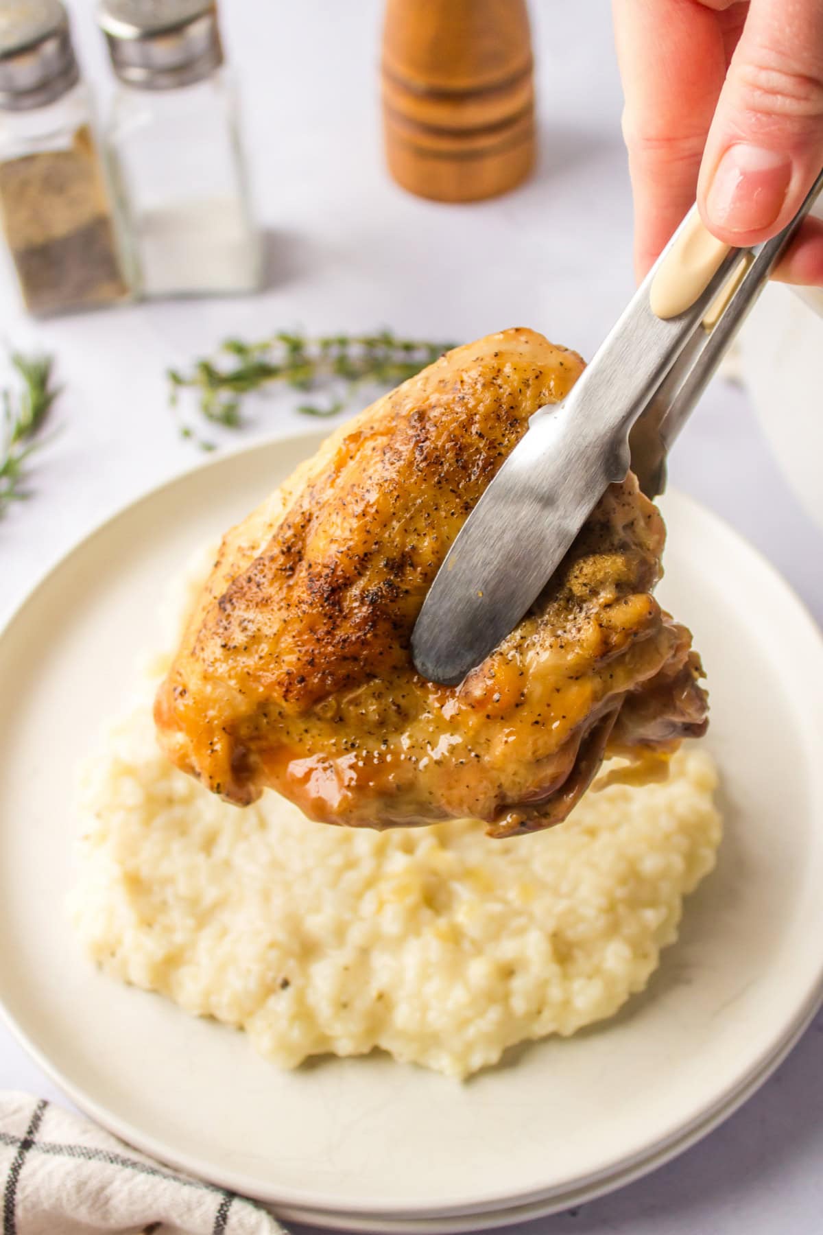 tongs putting chicken on top of risotto