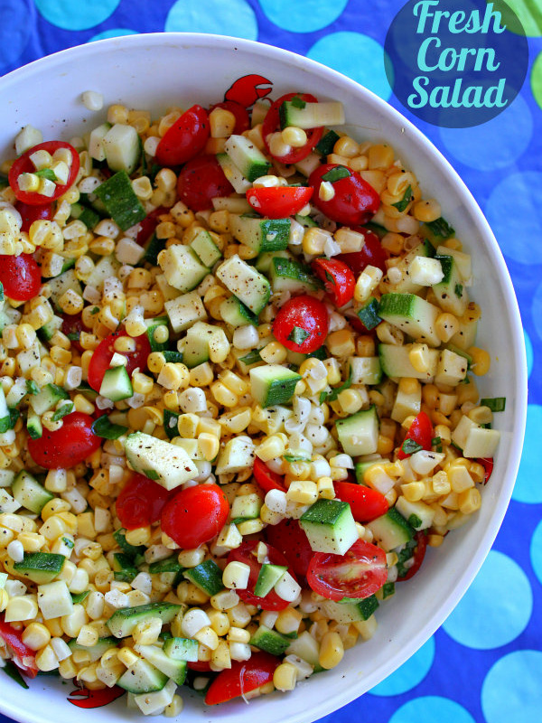 overhead shot of fresh corn, tomato and zucchini salad in a white bowl, set on a blue and green striped tablecloth