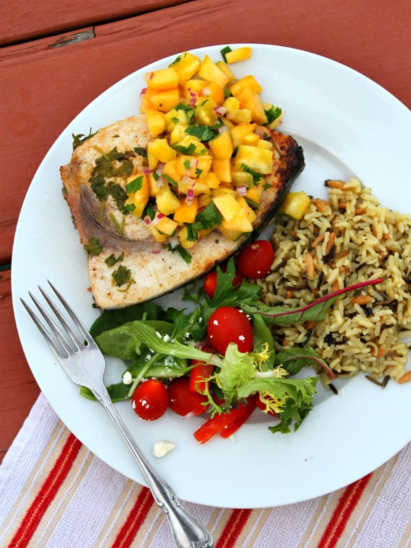 grilled swordfish with pineapple peach salsa and salad and rice on a plate