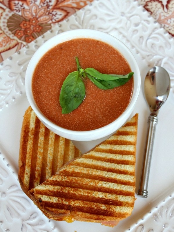 bowl of tomato soup with fresh basil and grilled sandwich on side