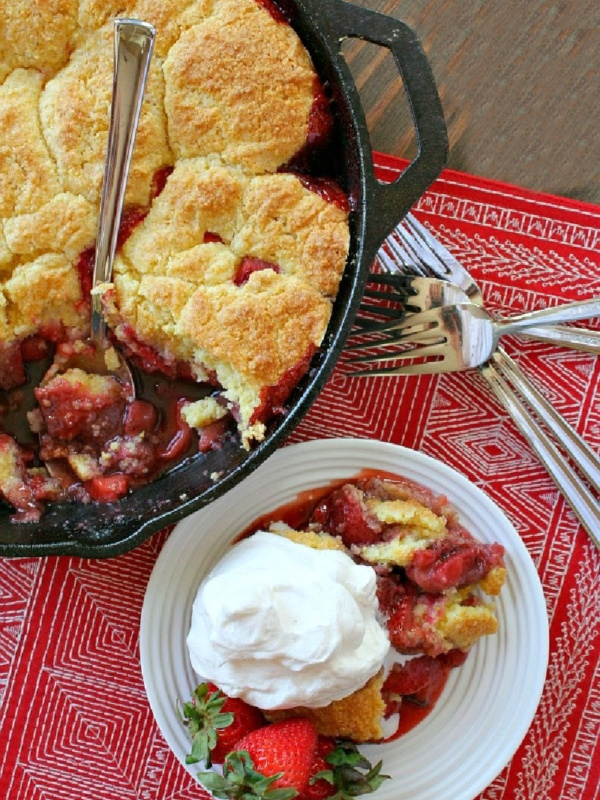 strawberry shortcake skillet cobbler in black skillet with serving of cobbler with cream on the side