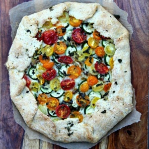 overhead shot of rustic tomato and zucchini tart on parchment paper sitting on a wooden cutting board