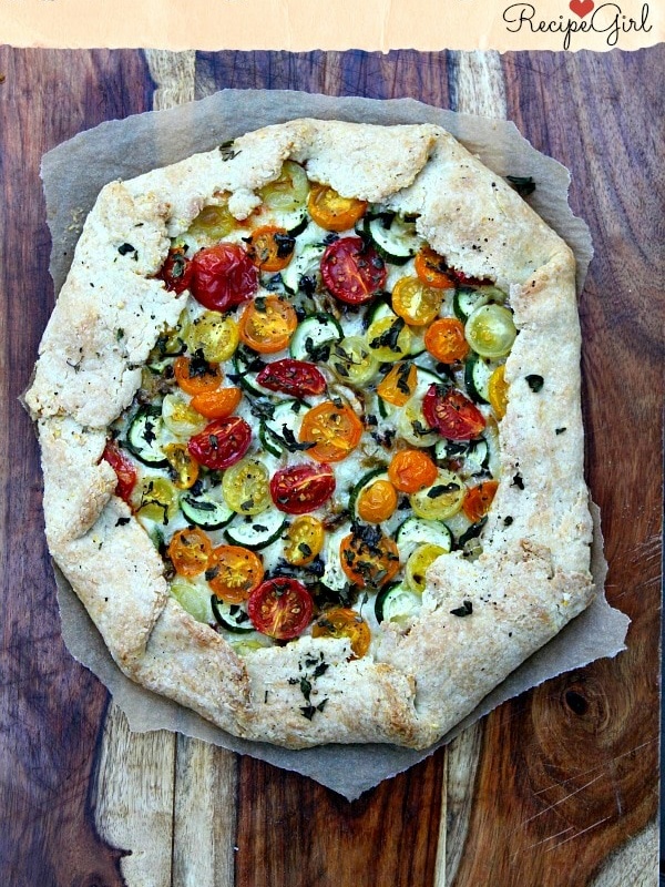 overhead shot of rustic tomato and zucchini tart on parchment paper sitting on a wooden cutting board