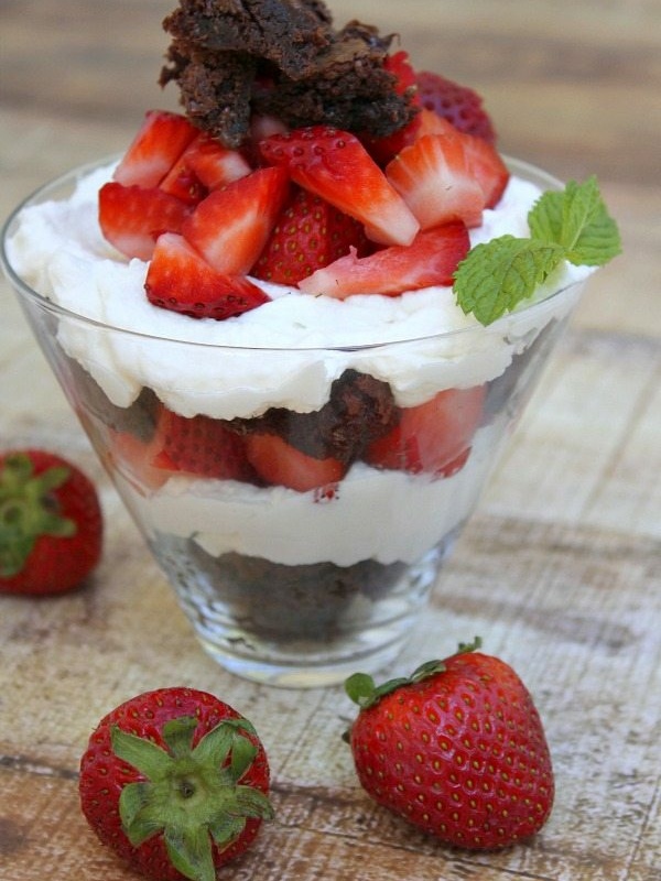 brownie strawberry shortcake in a clear glass with fresh strawberries scattered around