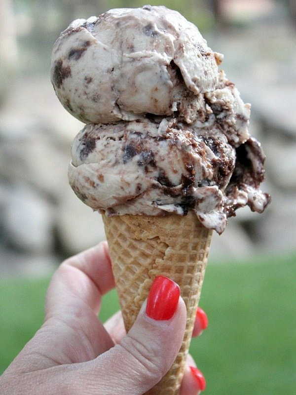 toasted marshmallow brownie malt ice cream scoop on a sugar cone with a hand holding the cone