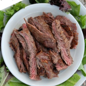 overhead shot of marinated grilled and sliced skirt steak on a white plate surrounded by lettuce leaves