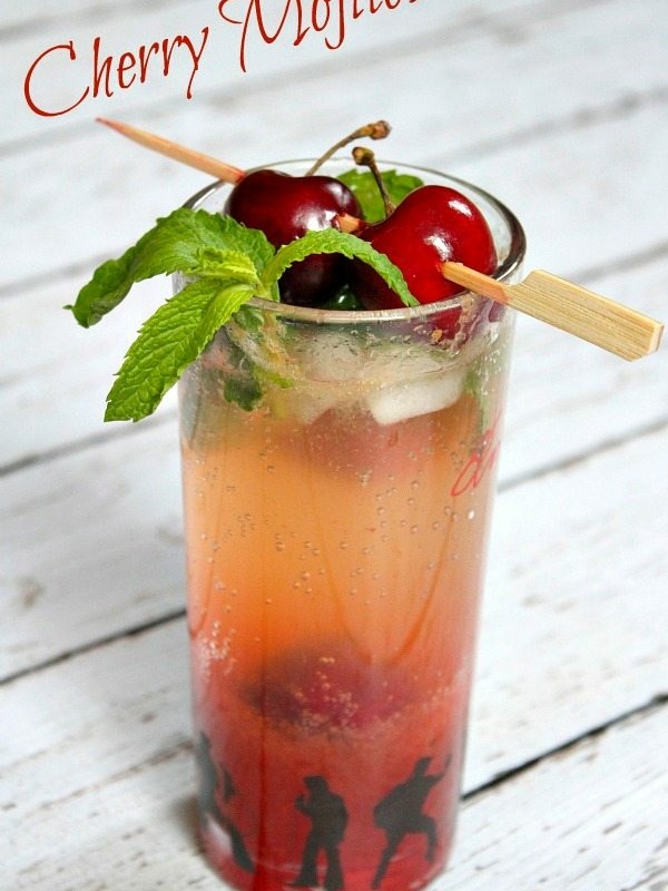 cherry mojito displayed on a white wood plank surface garnished with fresh cherries and mint