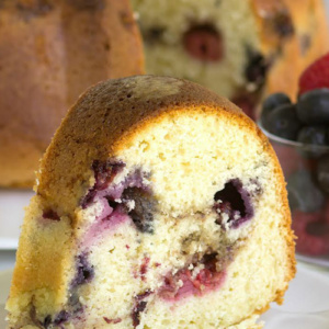 slice of two berry coffee cake on a white plate in front of the rest of the coffee cake