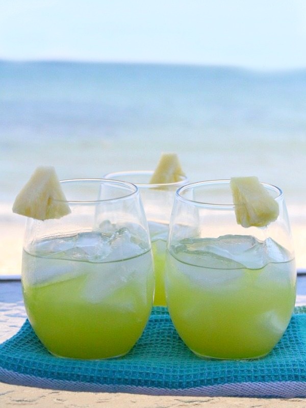 two pearl harbor cocktails sitting side by side garnished with pineapple sitting on a blue towel with the ocean in the background