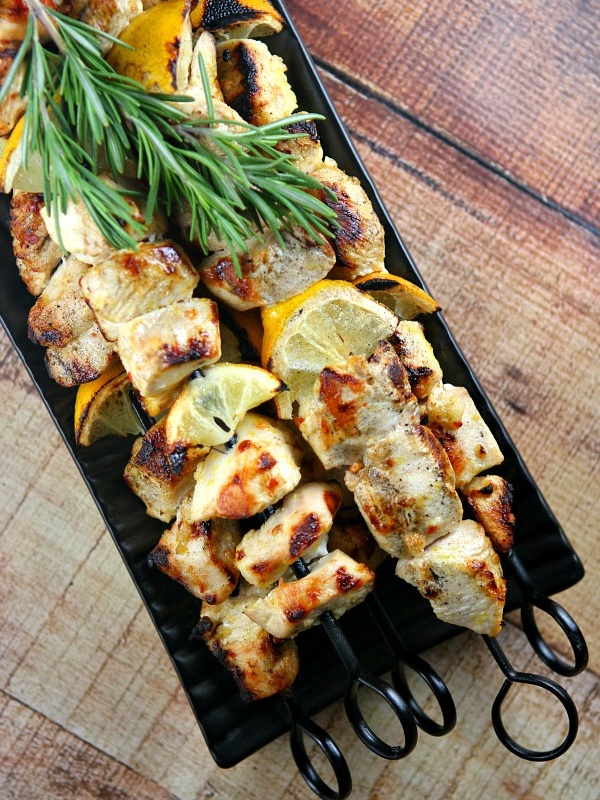 Rosemary lemon chicken skewers on a black tray with fresh lemon and fresh rosemary garnish