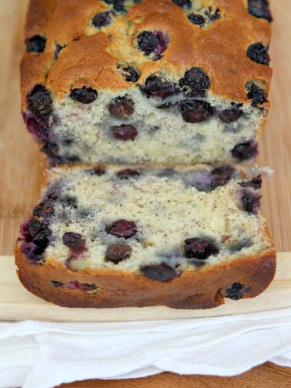 loaf of banana blueberry bread sliced open to see the inside on a cutting board