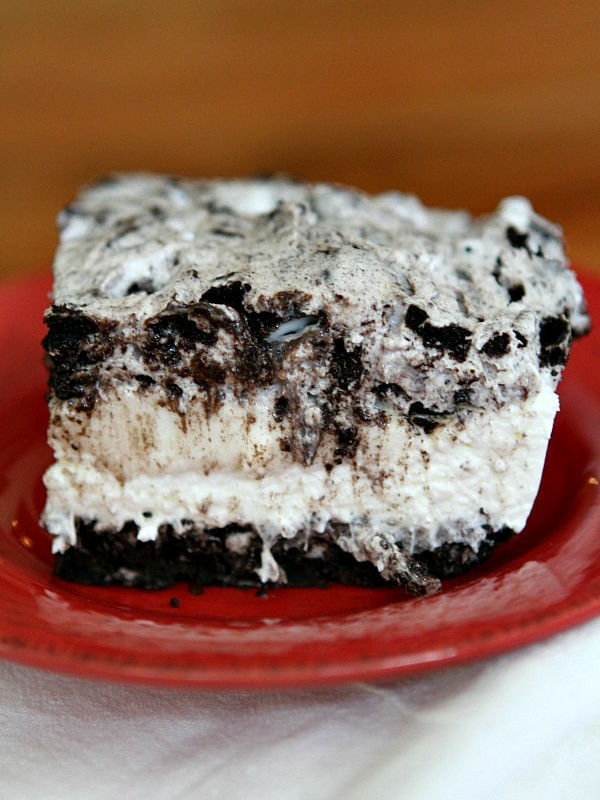 slice of no bake oreo cheesecake bar on a red plate on top of a striped white cloth napkin