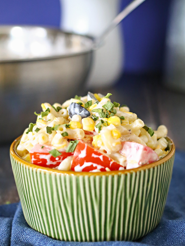 Summer Macaroni Salad in a green bowl sitting on a blue cloth napkin with a stainless steel bowl in the background