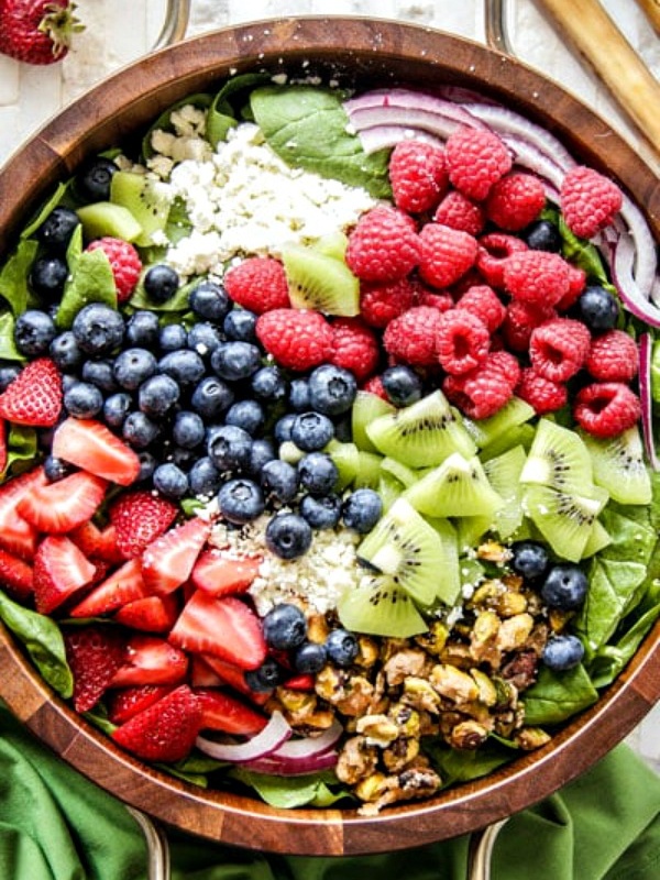 Overhead shot of kiwi berry salad in a wooden salad bowl with a green cloth napkin on the side