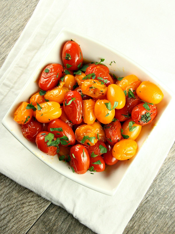 overhead shot of sauteed tomatoes with thyme in a white bowl garnished with fresh parsley sitting on a white cloth napkin