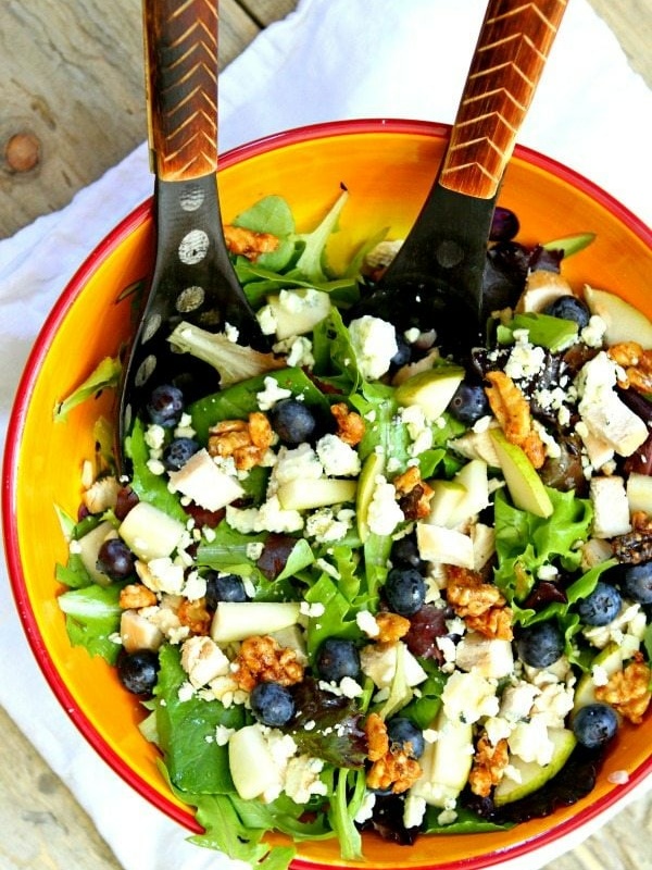 blueberry, blue cheese and glazed walnut salad in a yellow bowl with salad servers