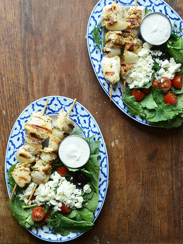 greek chicken kebabs plated with greek salad and sauce