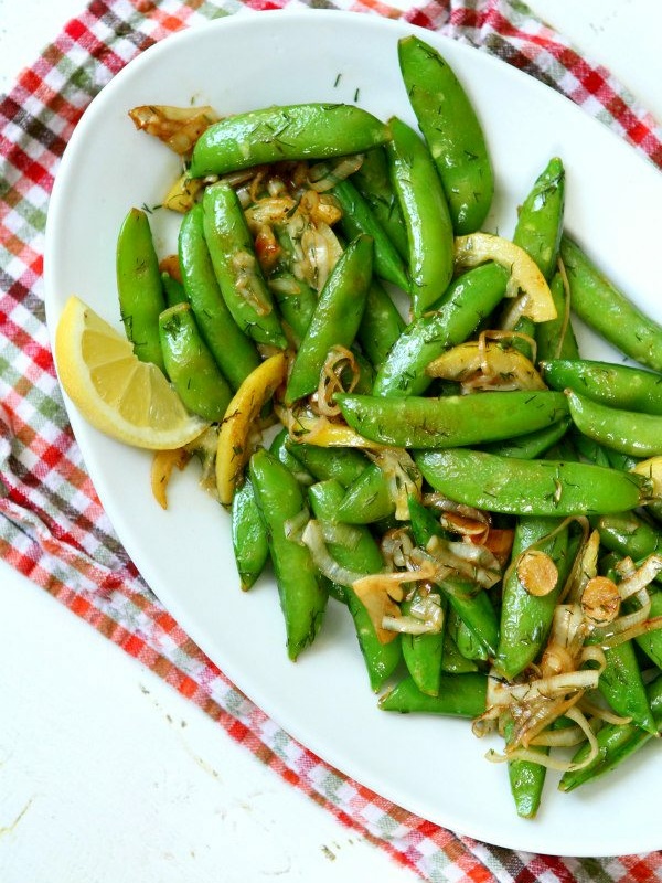 lemony stir fried sugar snap peas on a white serving platter set on a checked cloth napkin